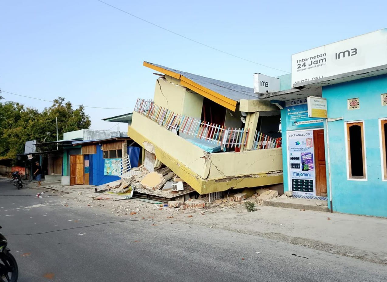 A two-storey shophouse collapsed forward onto the street, its upper floor balcony resting on the rubble of the ground floor.